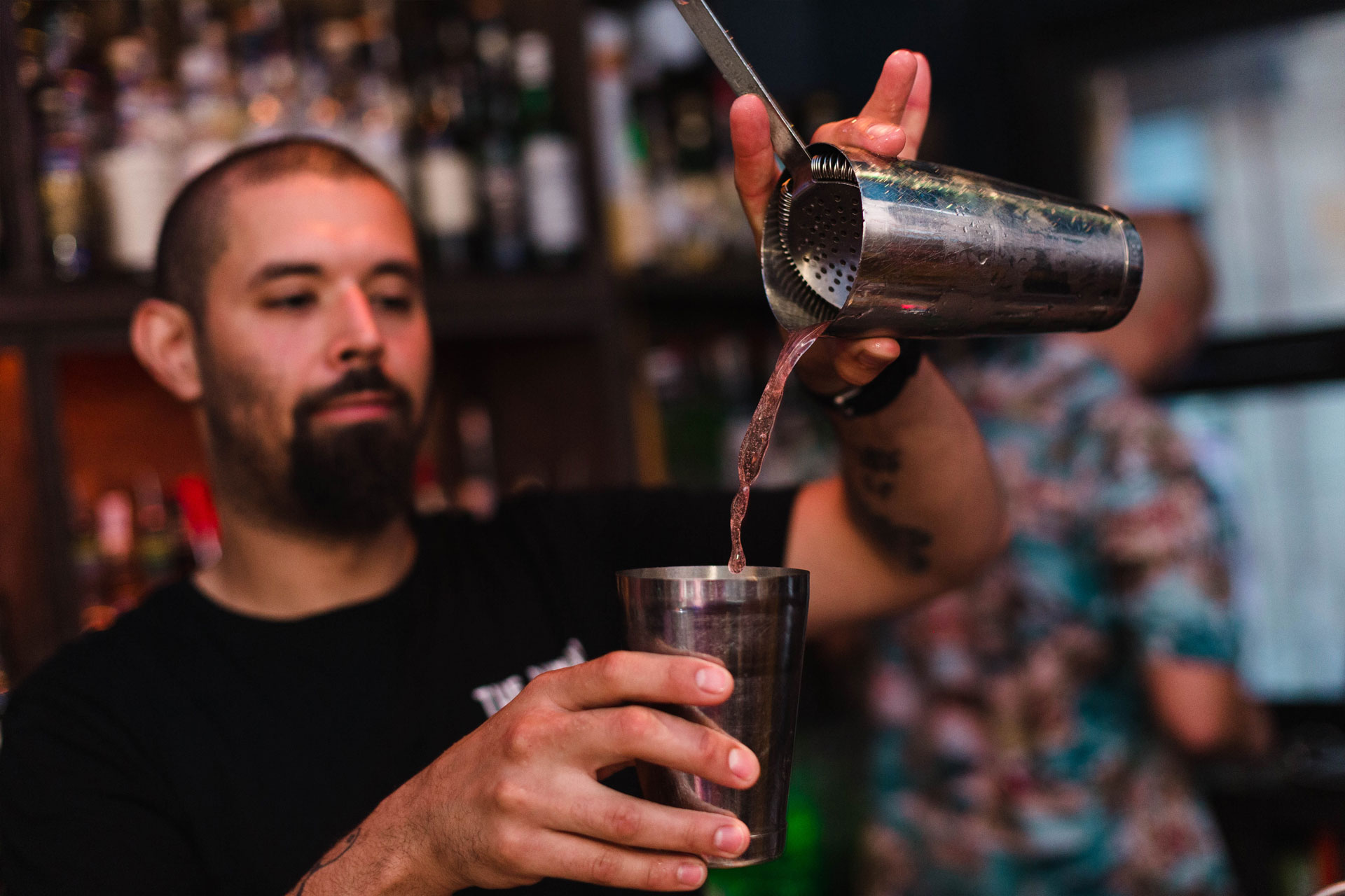 hombre joven con barba prepara un coctel y se ve caer el liquido