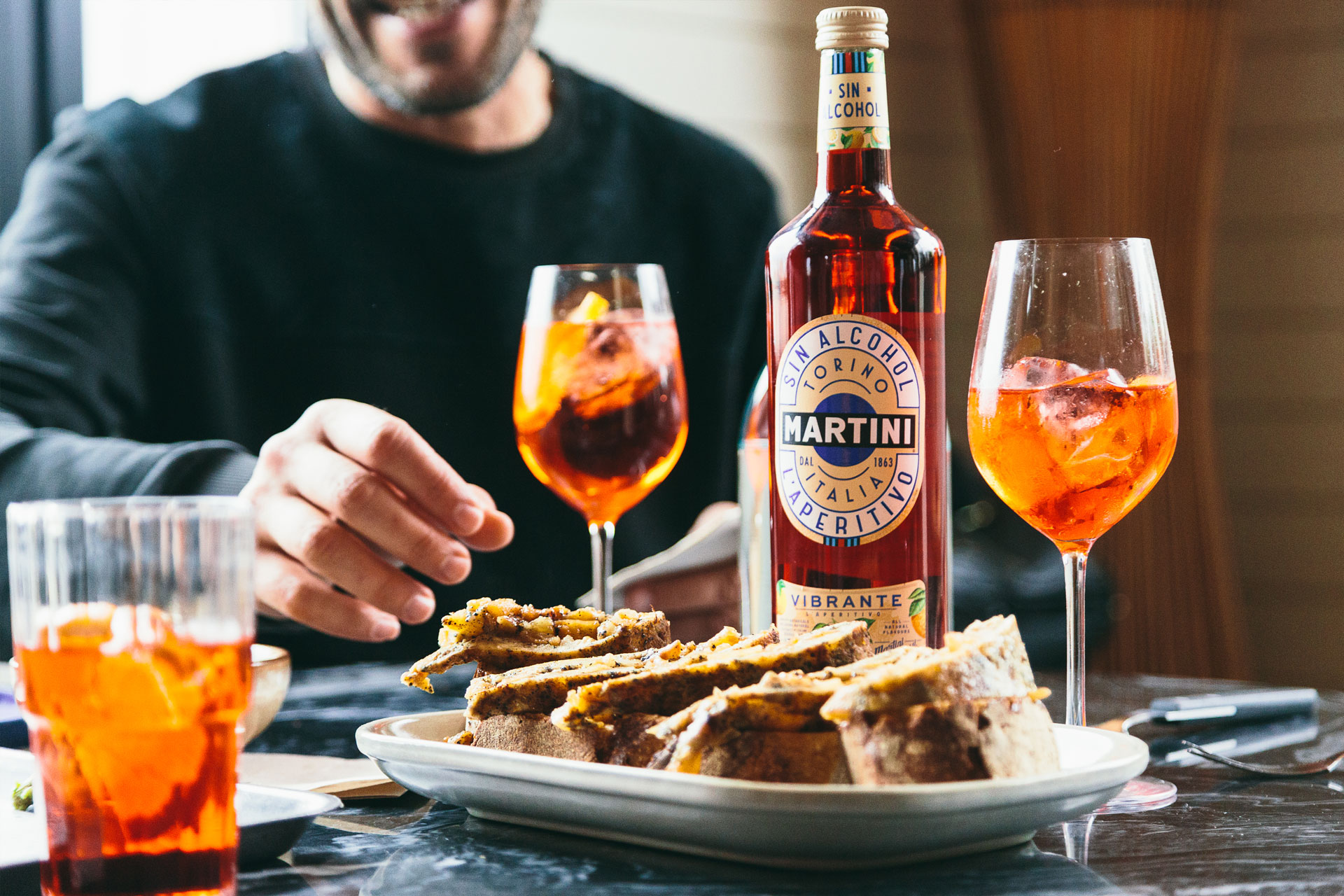 tapa de tortilla con dos copas y un vaso de aperitivo y en medio la botella de aperitivo martini sin alcohol