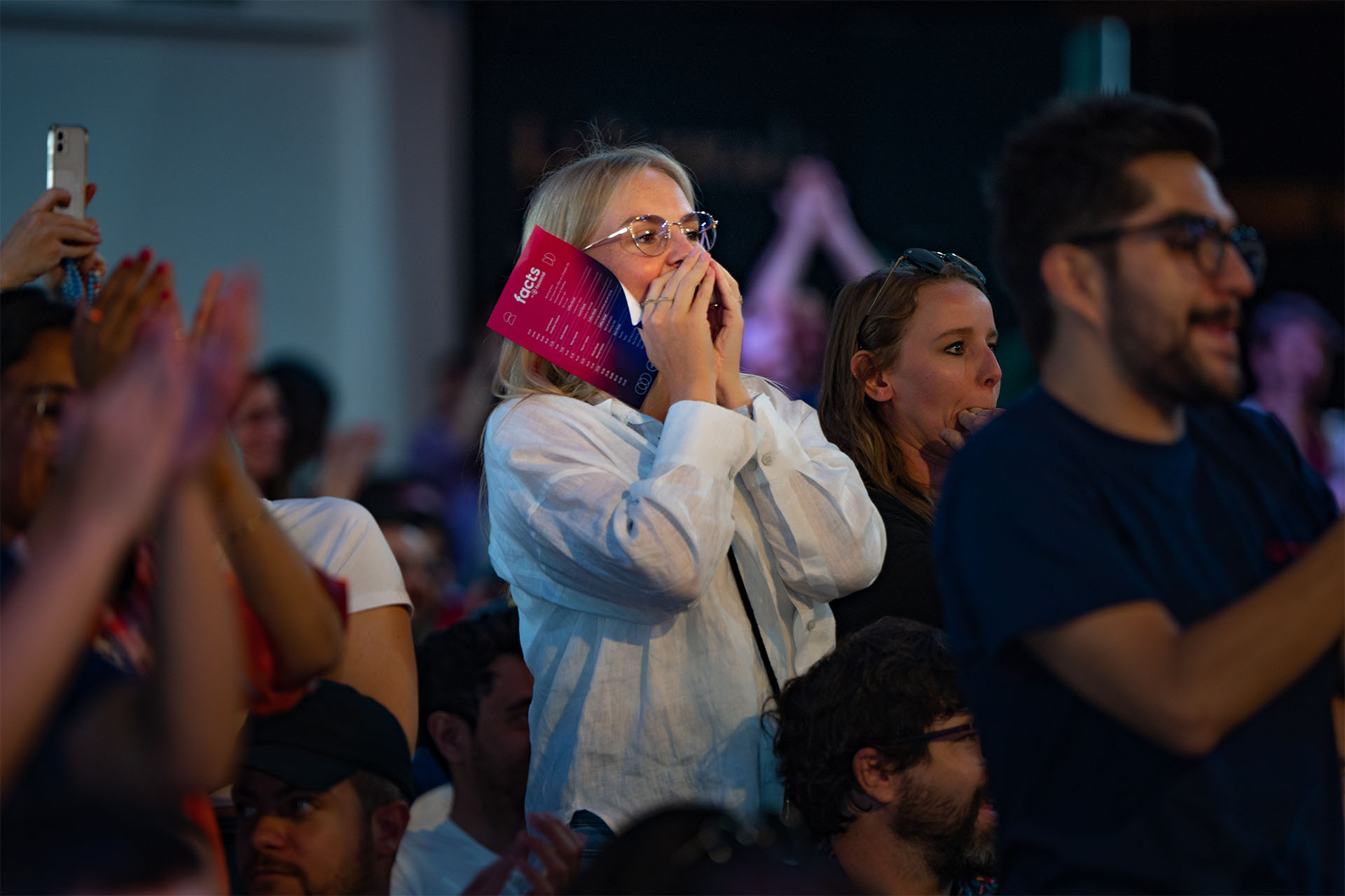 mujer joven con gafas entre el publico con las manos cubriendo la boca y haciendo ruido alabando la actuacion