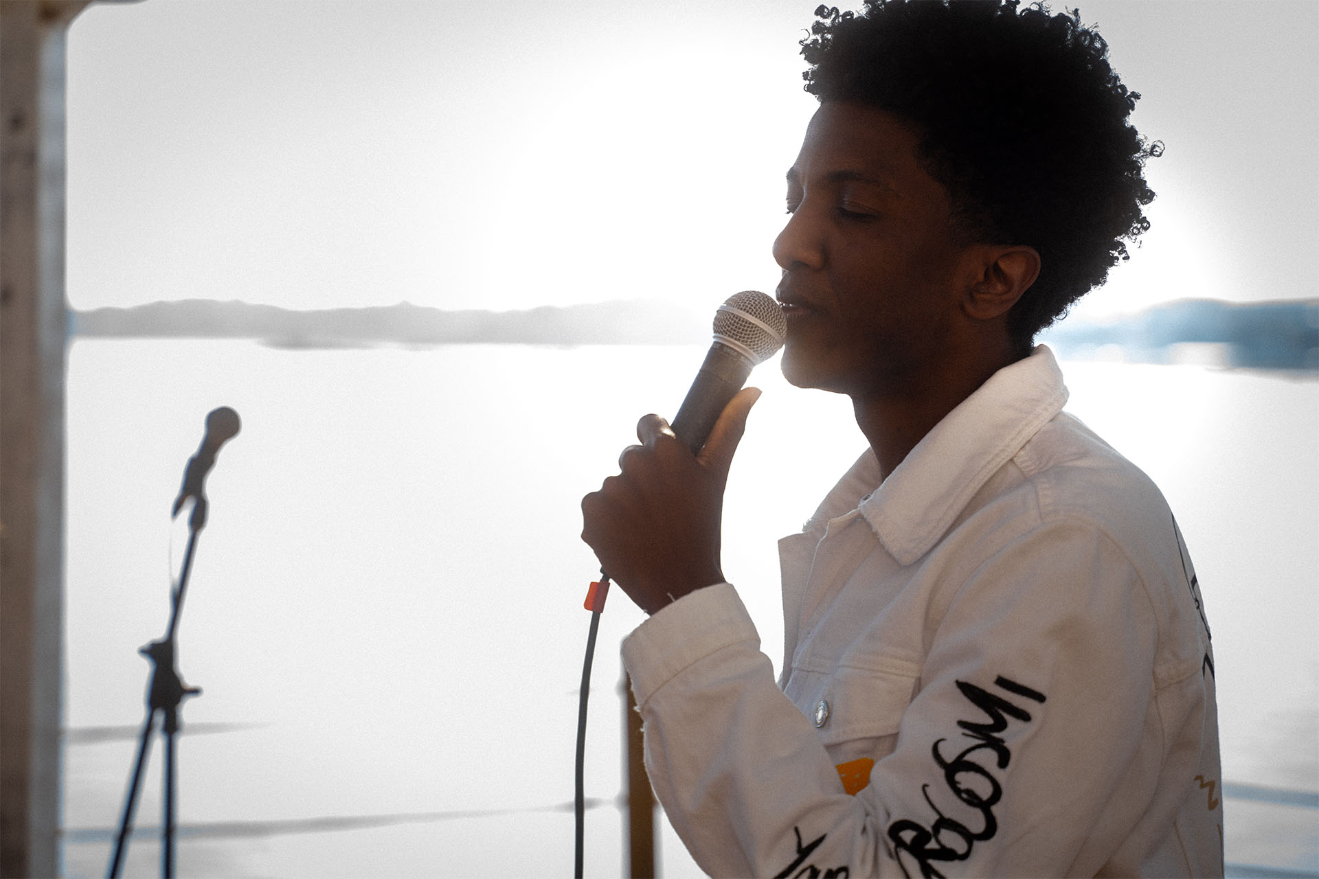 cantante de pie con los ojos cerrados en una playa con luz del sol detras