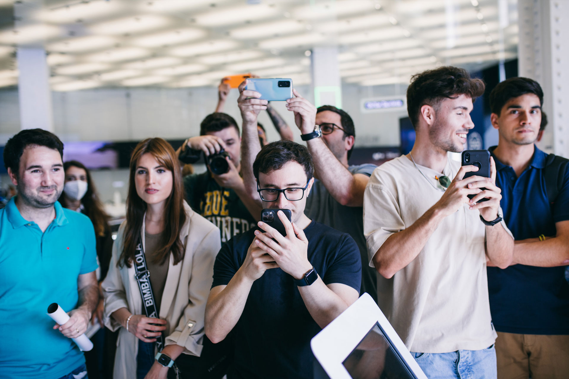 chico joven entre varias personas mirando a un movil y varias personas haciendo una fotografia